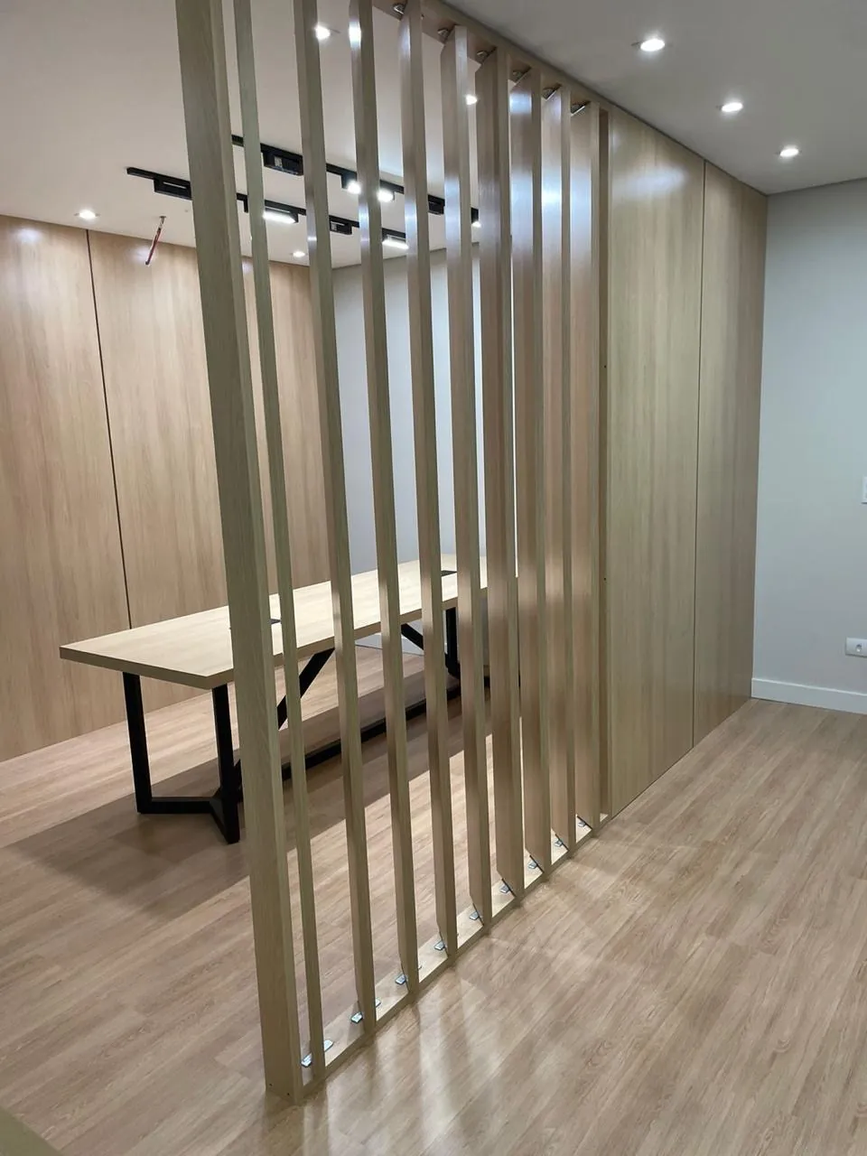 Divisória em ripado de madeira separando sala de reunião, com painéis amadeirados